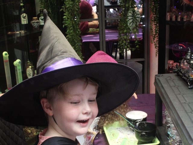 A child in a witch hat and cloak laughing at the potion table